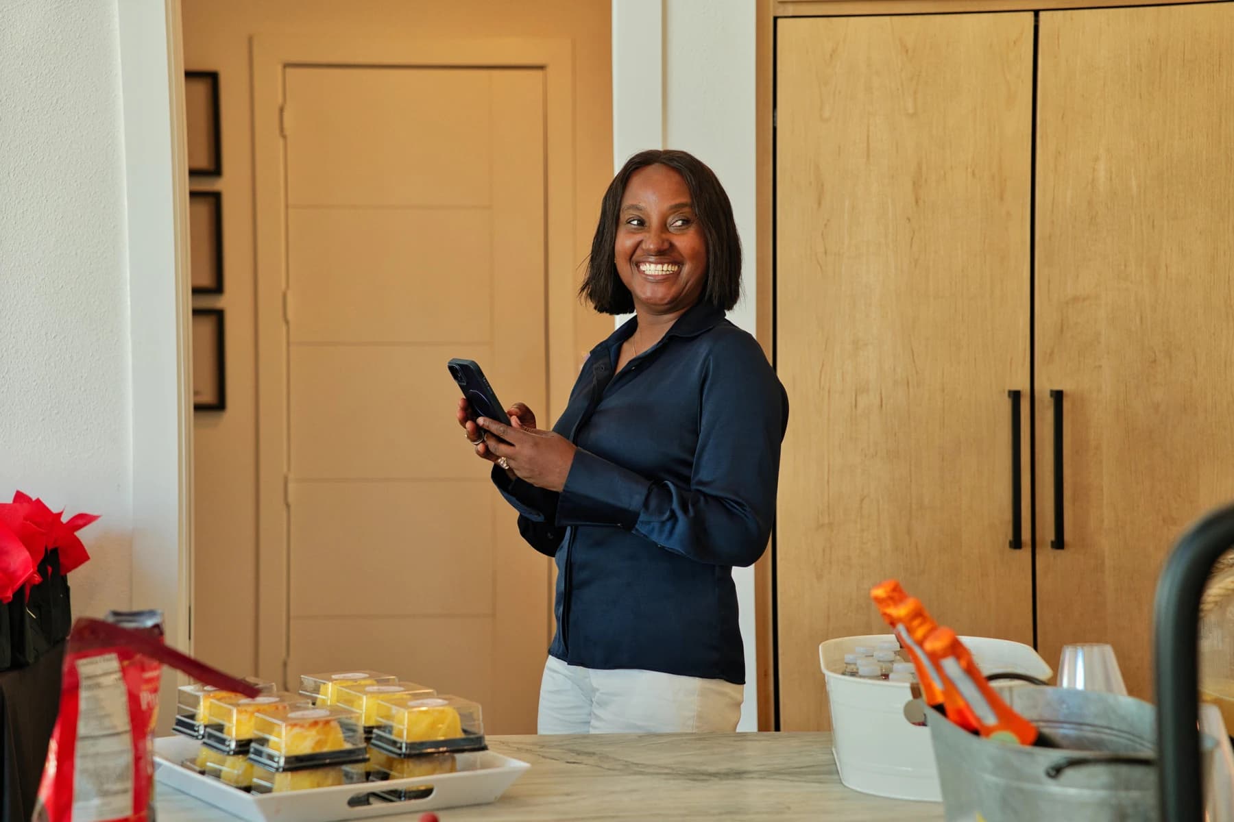 Esther Atere smiling while holding her phone in a home kitchen